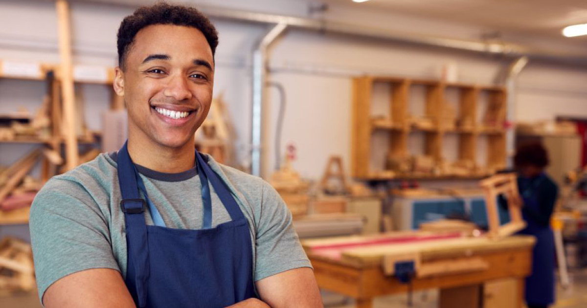 A young person in a woodworking shop, smiling.