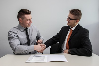 Two men in suits shaking hands at the table with a document in front of them