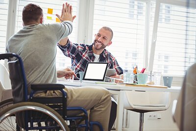 A person who is a wheelchair user high fives another person across a desk.
