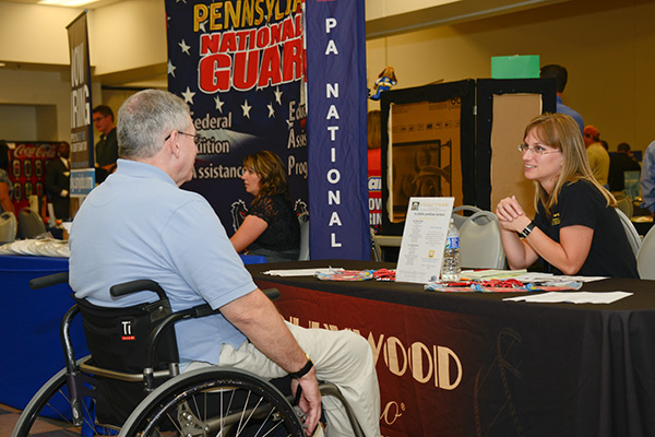 Photo of man in wheelchair speaking with potential employer at job fair