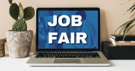 A laptop computer with the words “Job Fair” on a blue background on the screen. To the left is a cactus. 