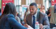 Two people talking to each other across a table at a job fair. 